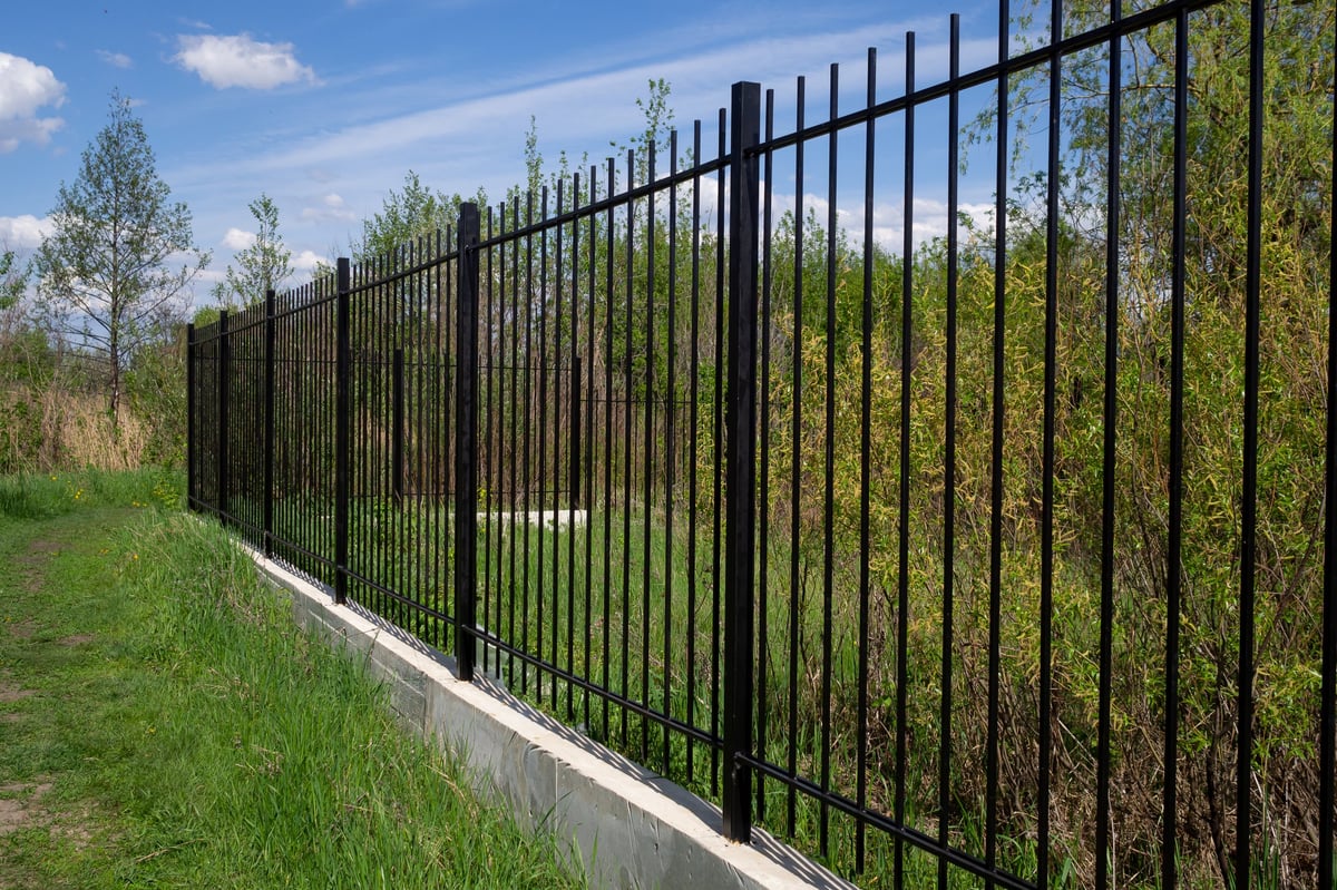 Long black iron panel fence with concrete foundation against a blue Texas sky