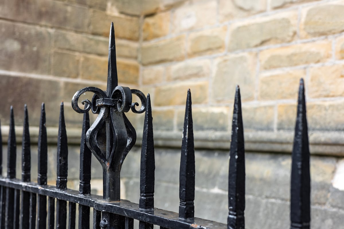 Ornate black wrought-iron fence railing with decorative finial on a stone wall