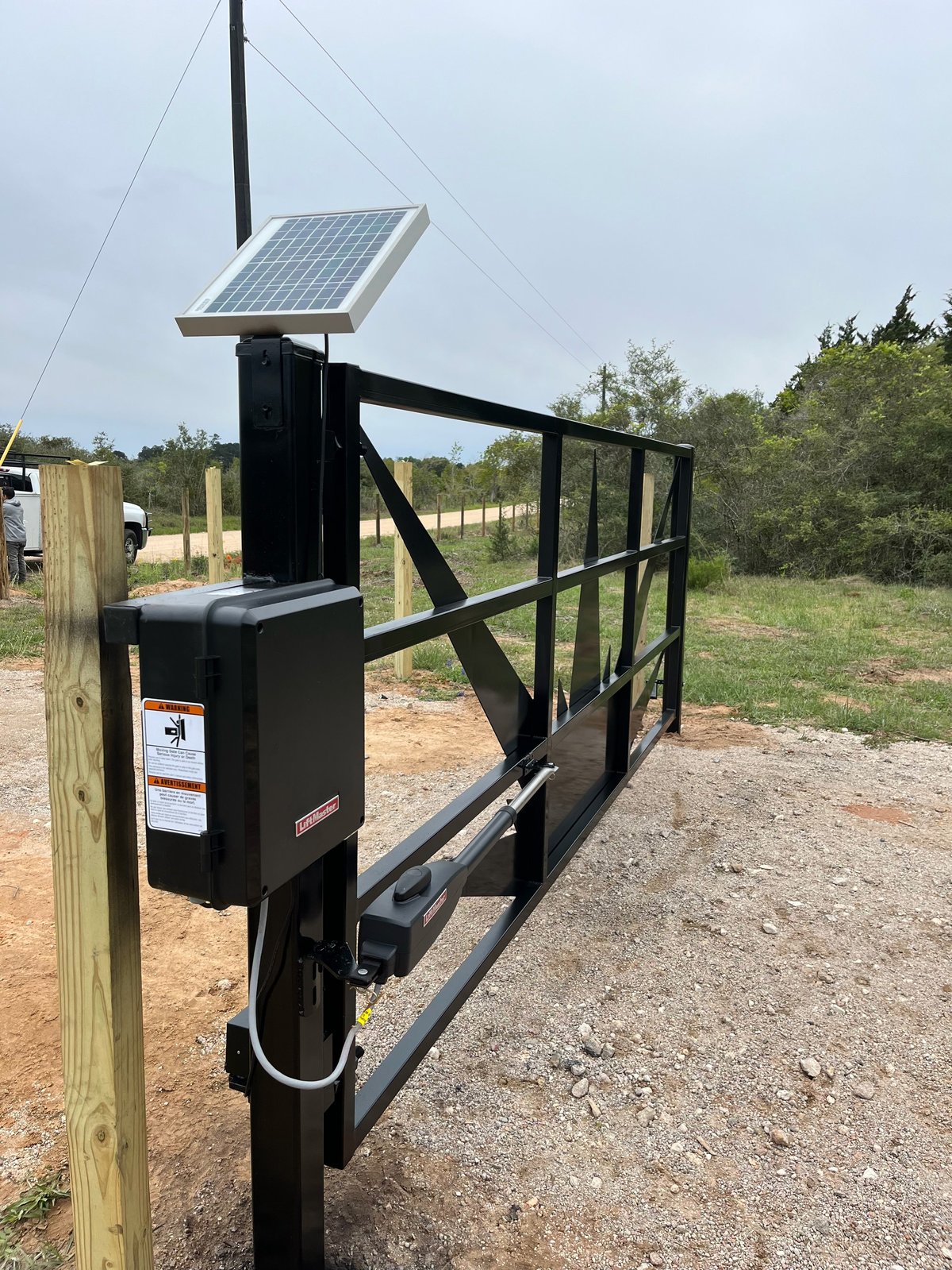 Solar-powered electric gate opener mounted on a black metal ranch gate