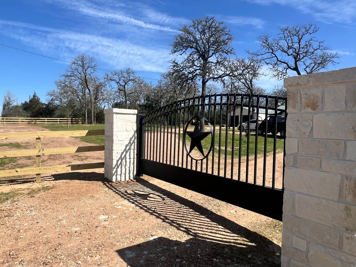 Black metal gate at a ranch property entrance with bare trees and rural landscape