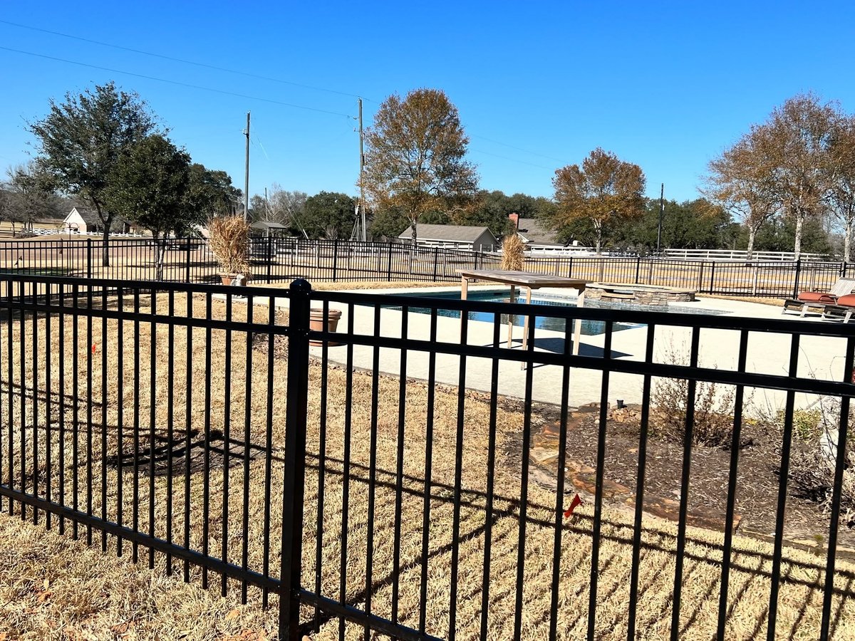 Black metal fence panels installed around a pool area with rural Texas property in background