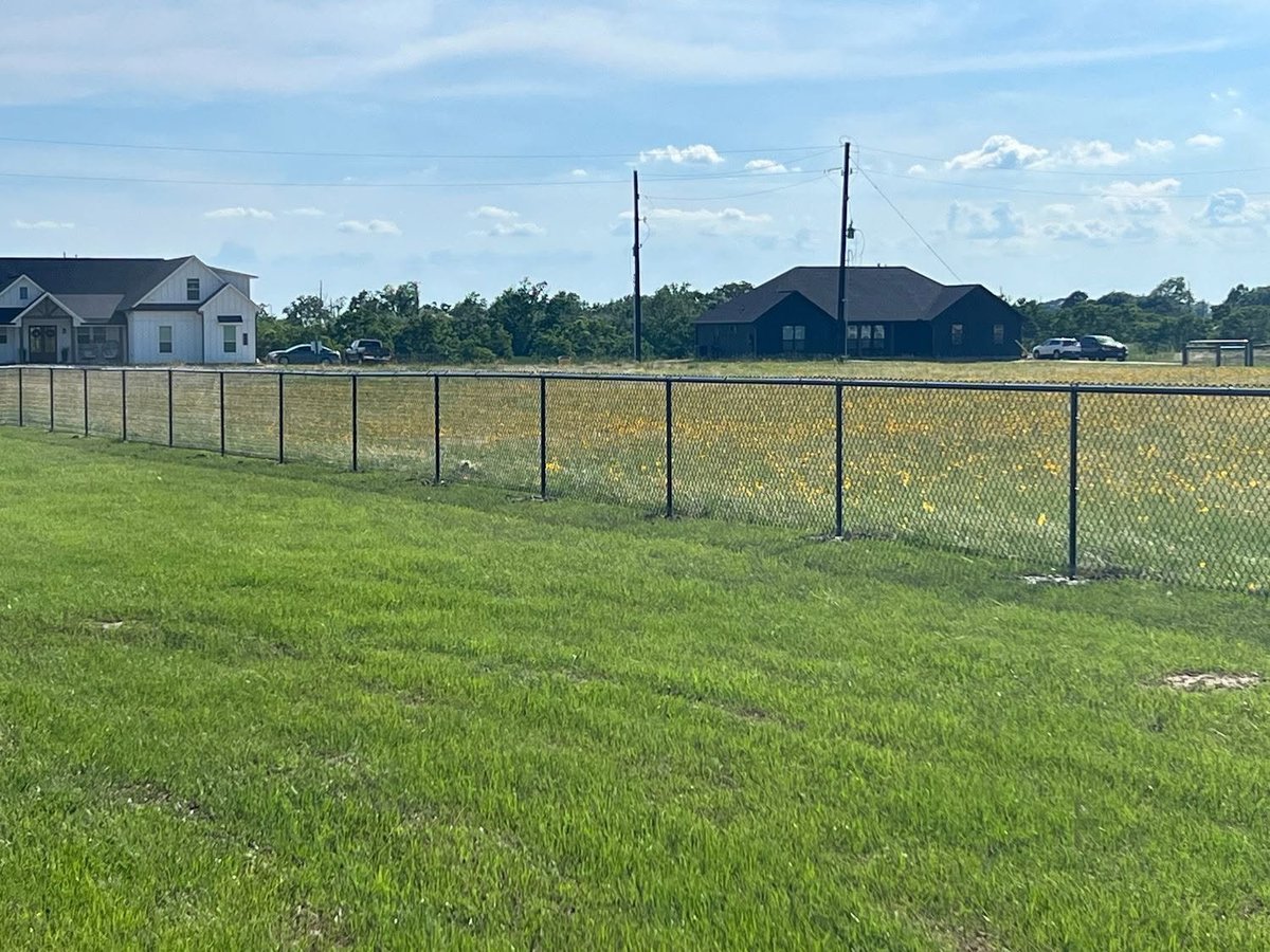 Chain-link fence running along a green grass field in a Brookshire TX neighborhood