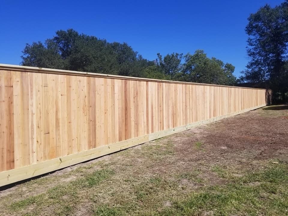 New wooden privacy fence installed along grassy yard with trees and clear blue sky in background