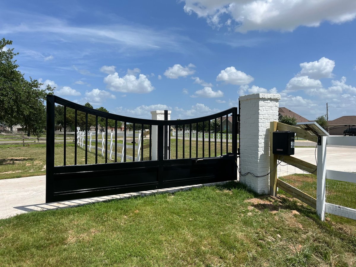 Black curved driveway gate with white fence post on a residential property