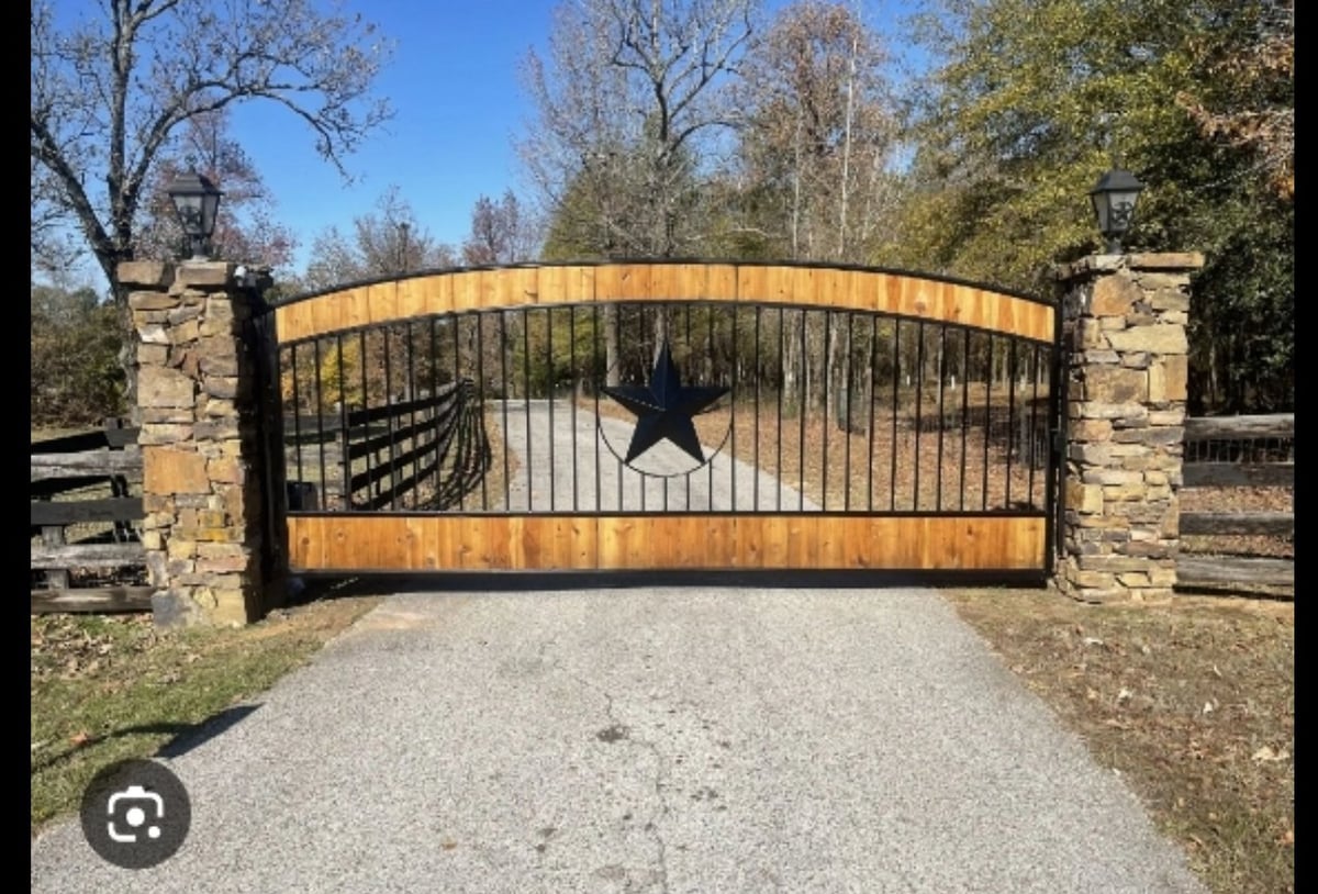 Ornate wood and metal driveway gate with a Texas star cutout, flanked by stone pillars