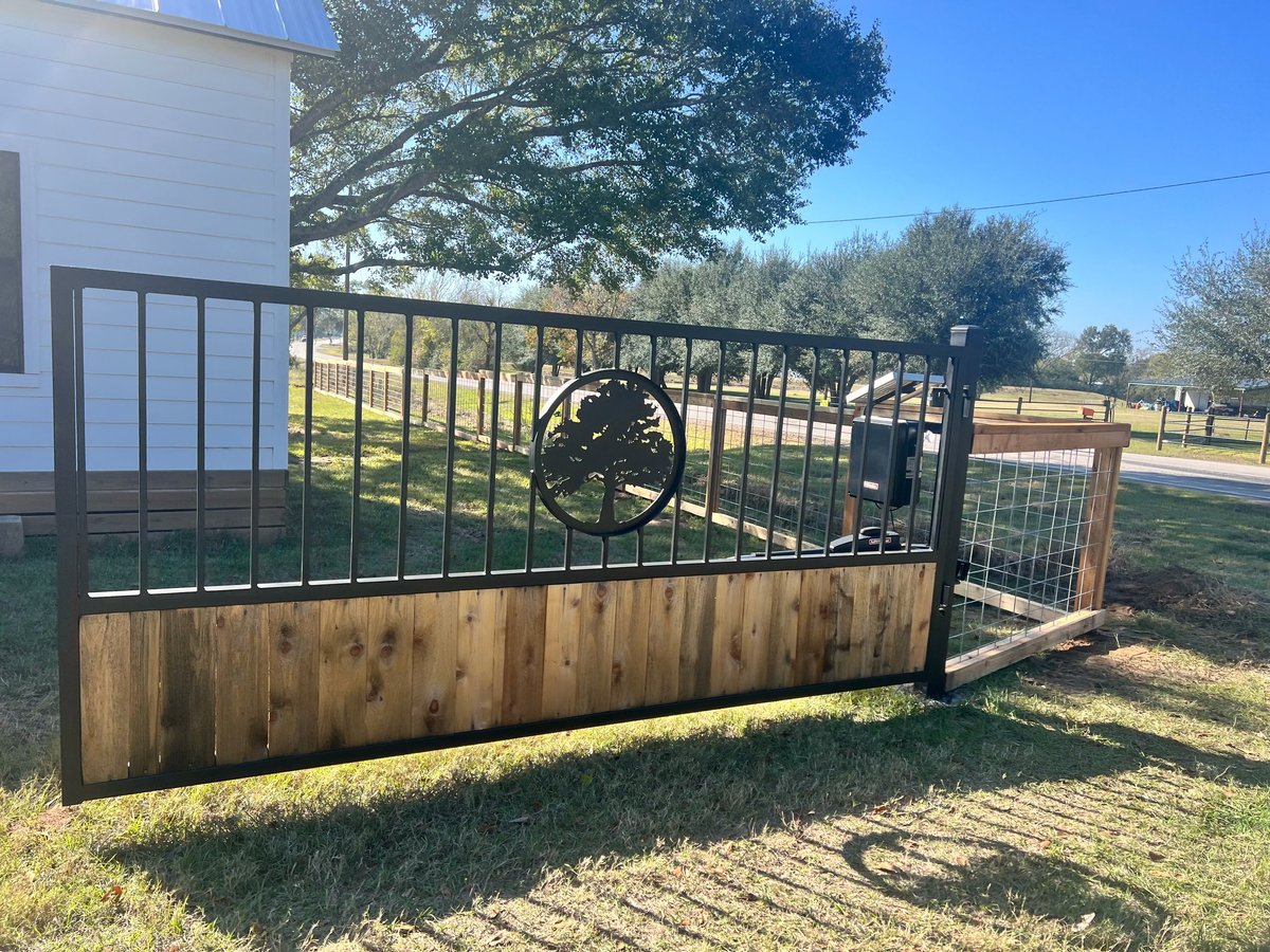 Metal and wood farm gate with a large tree-of-life wheel mechanism in a grassy yard
